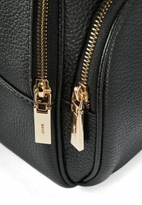 Czarna torebka z teksturowanej skóry z dwoma złotymi suwakami i prostokątnymi uchwytami suwaków, z przeszyciami wzdłuż szwów.