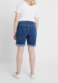 Keski siniset farkkushortsit, joissa käännetyt lahkeet, kaksi takataskua ja vyötäröllä nahkainen merkkilappu. Yhdistetty valkoiseen t-paitaan.