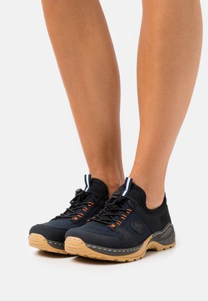Chaussures de sport noires avec des accents orange, tige en mesh, semelle en caoutchouc et lacets élastiques. Elles présentent un col rembourré et un branding sur le côté.