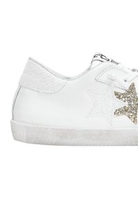Sneaker bianco con stelle di glitter bianche e oro sui lati e una suola graffiata e sporca.