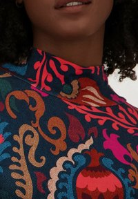 Kleurrijke geprinte stof met een blauwe achtergrond en ingewikkelde bloem- en scrollpatronen in roze, rood, oranje en groene tinten.