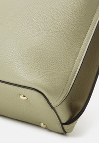 Světlé zelené kožené kabelka s texturovaným povrchem. Obsahuje zlaté kovové doplňky a černé lemování podél okrajů.