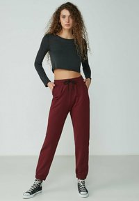 Schwarzes, kurzes Langarm-Shirt und kastanienbraune Jogginghosen mit elastischem Bund und Kordelzug, mit cuffed Knöcheln, getragen mit schwarzen Sneakers.