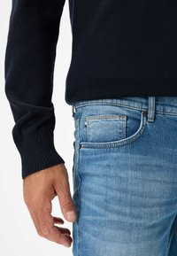 Maglione blu navy a maglia con polsini a coste abbinato a jeans in denim blu chiaro. I jeans presentano un lavaggio sbiadito e un dettaglio di tasca a toppa.