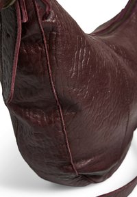 Sac à main en cuir bordeaux avec une surface texturée, une forme courbée, des coutures contrastées et une seule sangle pour le porter.