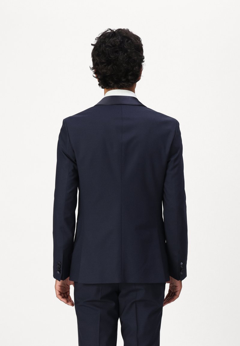 Veste de costume marine avec une coupe slim, fente simple et revers crantés. Présente quatre boutons aux poignets et une texture lisse.