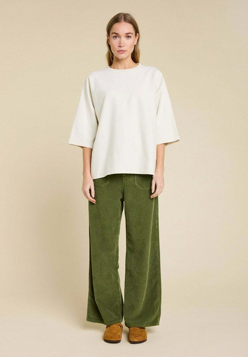 Un haut crémeux oversize avec des manches larges, associé à un pantalon large en velours côtelé vert. Des chaussures marron à enfiler complètent le look.