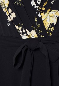 Vestido preto com um padrão floral em amarelo e branco, com um cinto na cintura e uma textura suave. Decote em V e detalhes de tecido plissado.