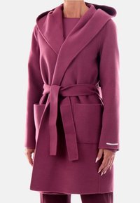 Cappotto lungo avvolgente in misto lana di un profondo colore rosa. Presenta un ampio cappuccio, cintura da annodare e due tasche frontali. Tessuto morbido e testurizzato.