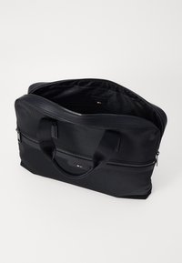 Sac à dos pour ordinateur portable noir en nylon texturé, avec des poignées doubles, une fermeture éclair et un intérieur spacieux avec un branding minimaliste.