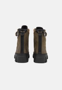 Stivaletti alla caviglia in suede verde con dettagli neri, dotati di suola spessa, chiusura con cerniera e hardware decorativo sul tacco.