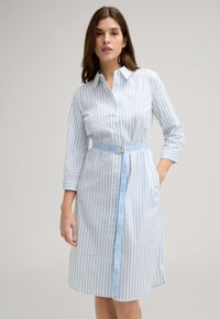 Abito camicia a righe blu chiaro e bianche con maniche lunghe, chiusura a bottoni sul davanti e una cintura con dettagli del logo. Include tasche laterali.