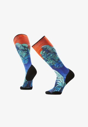 Skarpetki do kolan mają żywy niebiesko-pomarańczowy wzór z graficznymi motywami, czarne części na stopach i kostkach oraz gładką teksturę materiału.