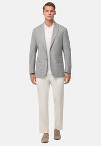 Siv houndstooth blazer z zareznimi lapelami, v kombinaciji z belo polo majico in smetanovimi hlačami, dopolnjen z bež loaferji.