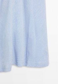 Tissu doux bleu clair avec une texture subtile, suspendu librement avec de légers plis sur un fond blanc.