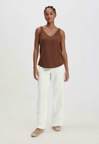 Bruine mouwloze top met V-hals, gecombineerd met witte wijde broek. De top heeft een zachte textuur; de broek is loose-fitting met een strakke uitstraling.