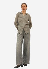 Grijze button-up shirt met twee borstzakken, gecombineerd met grijze wijde jeans en zwarte schoenen. Gladde stof met een ontspannen pasvorm.