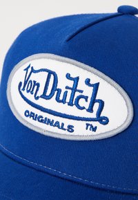 Kék pamut baseball sapka fehér ovális folttal, amelyen kék hímzéssel szerepel a "Von Dutch" és az "ORIGINALS" felirat, szürke varrási részletekkel. 