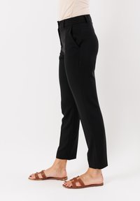 Pantaloni neri su misura con una vestibilità slim, caratterizzati da pieghe, una texture liscia e una lunghezza accorciata. Indossati con sandali a ciabatta marroni.