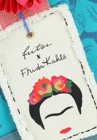 Etiqueta de tejido tejido con un diseño floral que presenta el rostro de una mujer, colores brillantes y bordes texturizados. Incluye un logotipo impreso y adornos.