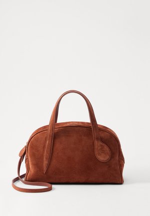 Brūnas zamšadas rokas soma ar noapaļotu formu, īsām rokām un noņemamu plecu siksnu. Iezīmē gludas akcentus un iešūtu aizdari.