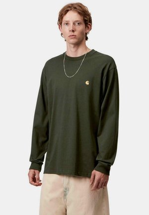 Camicia verde di cotone a maniche lunghe con una vestibilità rilassata, caratterizzata da un piccolo logo dorato sul petto e un colletto rotondo.