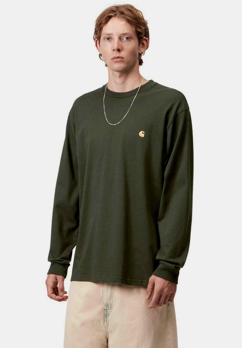 Camisa de algodón verde de manga larga con corte relajado, que presenta un pequeño logo dorado en el pecho y un cuello redondo.