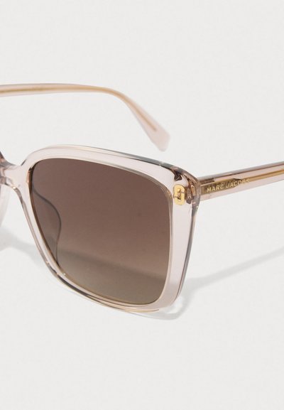 Duidelijke vierkante zonnebril met bruin getinte lenzen en gouden accenten, waaronder het Marc Jacobs-logo op de poot.