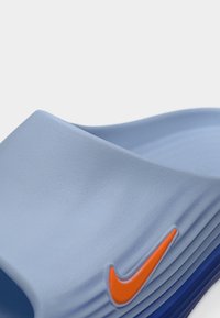 Sandale slide Nike bleu clair avec un logo Swoosh orange sur le côté et des détails de semelle rainurée.