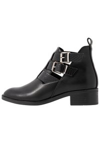 Stivaletto nero realizzato in pelle liscia con due cinturini regolabili a fibbia e un pannello texturizzato. Tacco basso a blocco e linguetta sul retro.