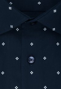 Dunkel marineblauer Hemdkragen und Knopfleiste mit einem Muster aus kleinen weißen Vier-Punkt-Clustern, gleichmäßig über den Stoff verteilt.