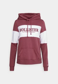 Sudadera burdeos con franja horizontal blanca, bolsillo canguro delantero, capucha con cordón y texto "Hollister Southern California" en el pecho.