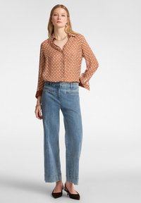 Camicia a maniche lunghe con motivo marrone, abbinata a jeans in denim a gamba larga di un blu chiaro e scarpe a punta di colore marrone scuro.