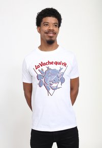 Hvid T-shirt i bomuld med et grafisk billede af et kvæges ansigt, fremhævet med fede, farverige linjer og teksten "La Vache qui rit" i rød.