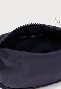 Tmavomodré plátené puzdro so zipsom. Vo vnútri je bielym písmom vytlačený nápis "TOMMY HILFIGER". Hladká textúra a minimalistický dizajn.