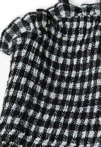 Haut en tissu à motif à carreaux noir et blanc avec un design froncé. Présente un col à volants et une surface texturée. Léger et ajusté.