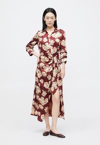 Długa bordowa sukienka w kwiaty z kołnierzykiem, z wiązanym w talii detalem i wysokim rozcięciem; wykonana z satyny o gładkiej fakturze.