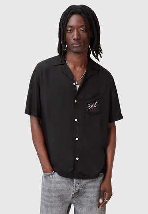 Camisa negra de manga corta en tejido ligero, con un bolsillo que tiene un bordado colorido de "LOVERS" y botones blancos.