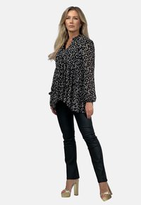 Czarna i biała kwiatowa bluzka z długimi rękawami i plisowanym wzorem, zestawiona z dopasowanymi czarnymi spodniami i złotymi platformami na obcasie.