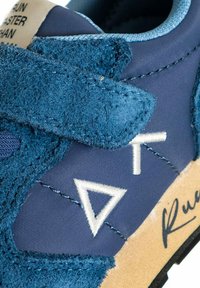 Sneaker blu caratterizzato da una combinazione di suede testurizzato e tessuto liscio. Presenta decorazioni ricamate bianche e una suola in gomma.