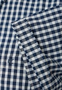 Marineblauwe en witte gingham kartering shirtdetail, met gladde katoenen stof, opgerolde manchetten en geborduurd logo op de borstzak.
