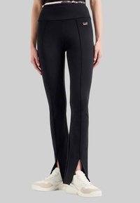 Zwarte sportleggings met een brede tailleband, met zijslits aan de zoom en een klein metalen logo aan de voorkant.