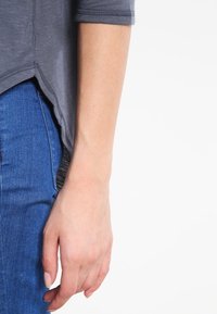 Grå t-shirt med kort ärm och rundad nederkant, i kombination med blå denimjeans. Slät tygkvalitet och kontrasterande sömmar är synliga.