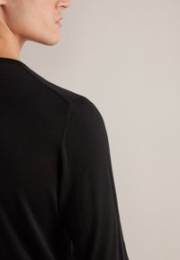 Maglietta nera a maniche lunghe in maglia con scollatura a girocollo, caratterizzata da una texture liscia e da una cucitura visibile sulla cucitura della spalla.