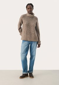 Beige pletený rolák s uvolněným střihem, s žebrovaným lemem, v kombinaci s světle modrými džíny rovného střihu a hnědými šněrovacími botami.