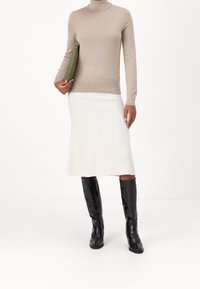 Bežový rolák, bílé úzké midi sukně s jemným žebrováním, černé kozačky po kolena s krokodýlím vzorem, zelená kabelka v ruce.