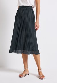 Pleated midi skirt in dark gray, featuring a wide waistband and flowing hem. Paired with silver strappy sandals for a complete look.