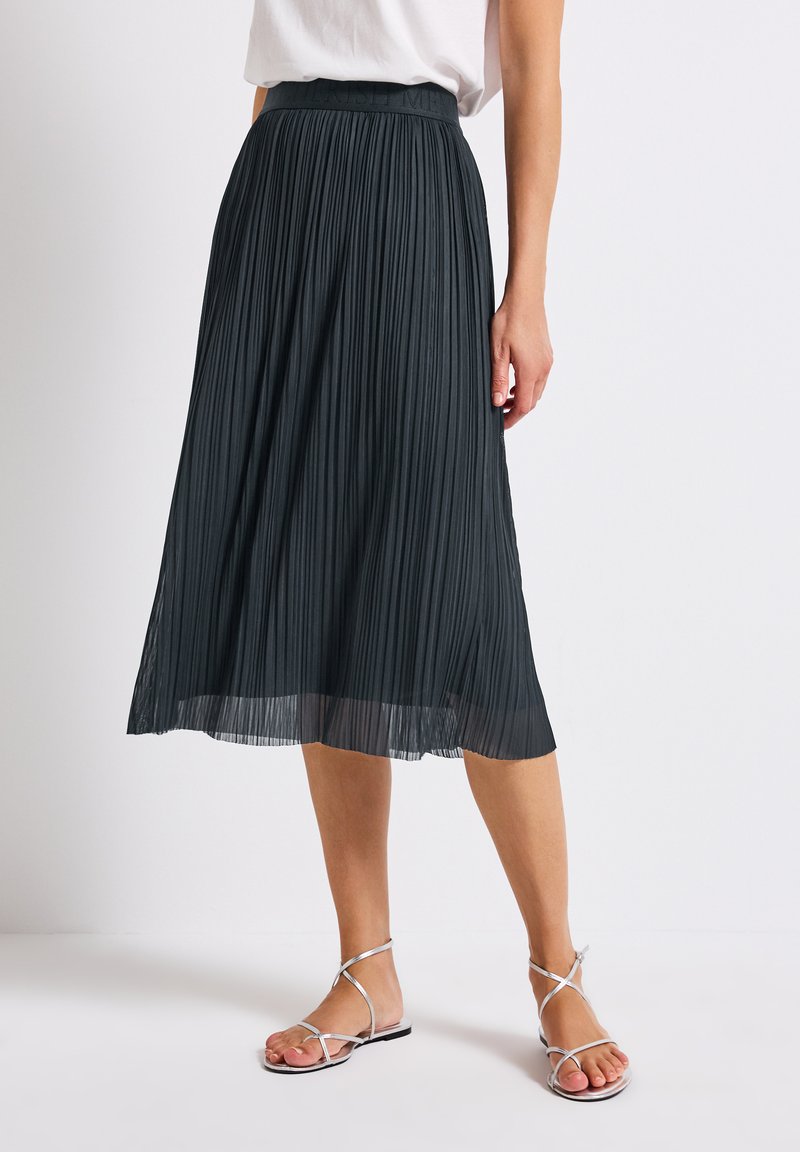 Pleated midi skirt in dark gray, featuring a wide waistband and flowing hem. Paired with silver strappy sandals for a complete look.