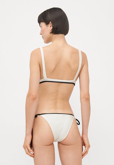 Divdaļīgs bikini krēmkrāsā ar melnu apdari. Augšdaļai ir vienkāršs dizains ar regulējamām siksnām, bet apakšdaļa ir ar sānu saitēm.