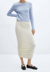 Lichtblauwe geribde trui, crèmekleurige midi-rok met geplooide details, en zwarte platte schoenen met strikaccenten. Eenvoudig, nauwsluitend ontwerp.